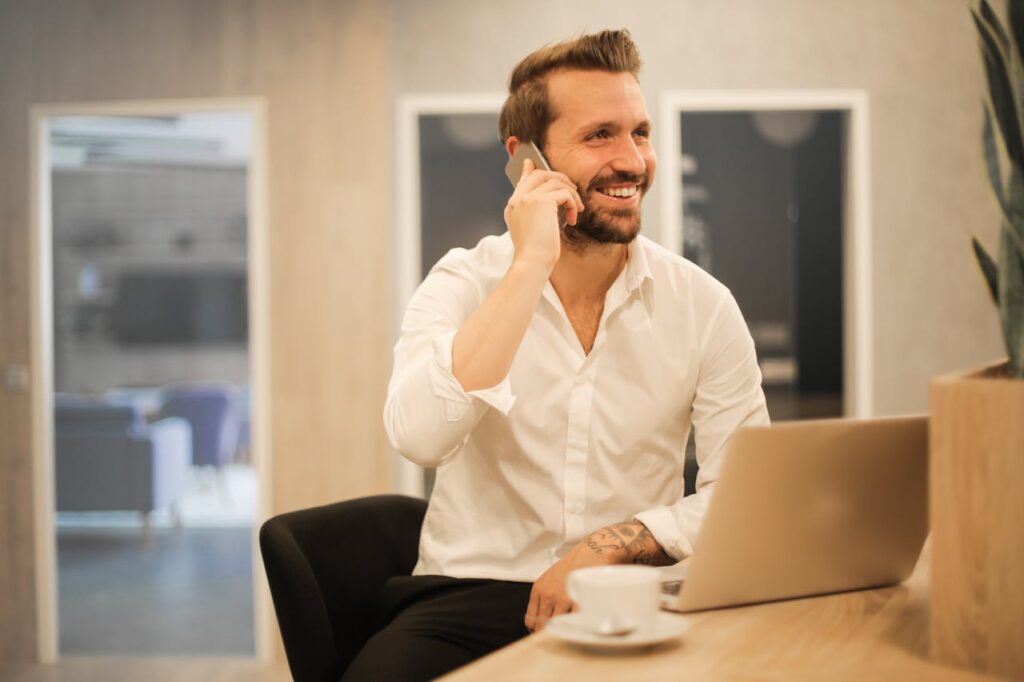 Smiling formal male with laptop chatting via phone